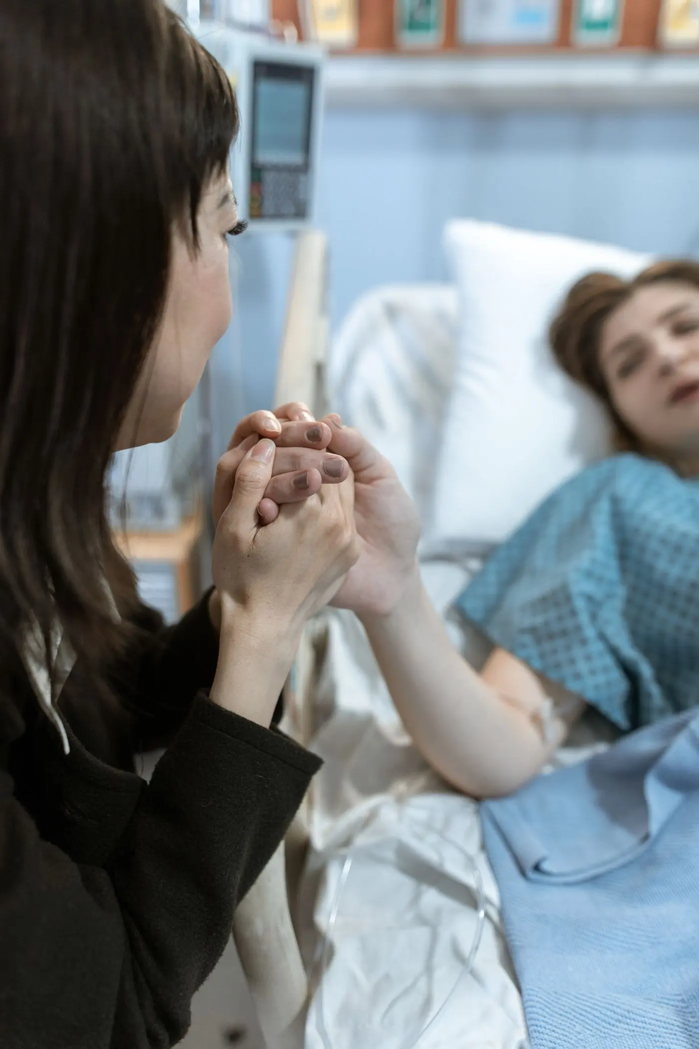 Una mujer toma la mano de una paciente hospitalizada, sentada junto a la cama